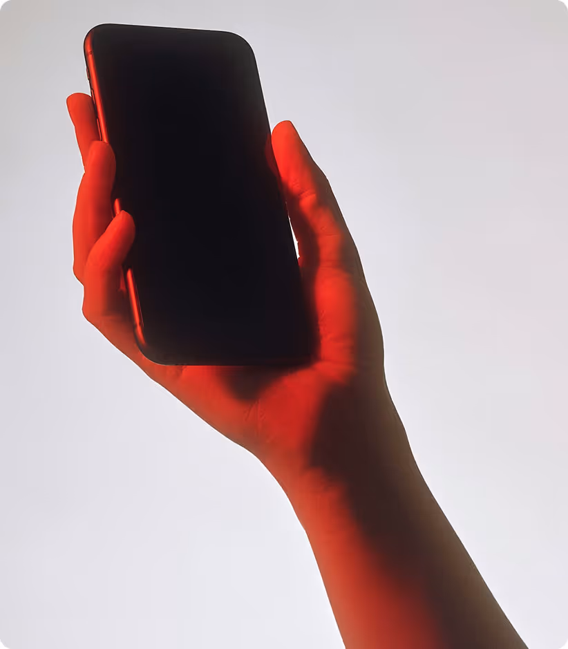 Main tenant un smartphone noir avec un éclairage rouge sur fond gris clair.