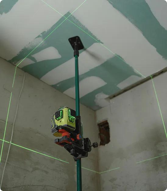 Niveau laser vert monté sur un trépied ajustable dans une pièce en rénovation avec murs partiellement peints.