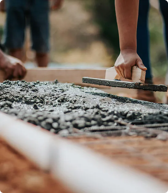 Une main lissant du béton frais avec une truelle lors d'un chantier extérieur.