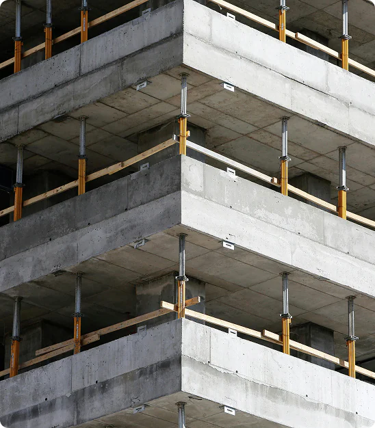 Angle d'un bâtiment en construction avec dalles en béton et supports métalliques jaunes.