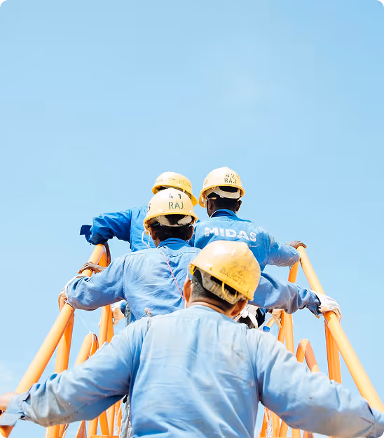 Quatre ouvriers en tenue bleue et casques jaunes montant un échafaudage orange sous un ciel bleu clair.