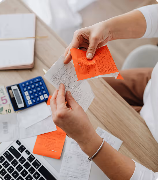 Person holding receipts with calculator, money, and laptop on table, organizing finances.