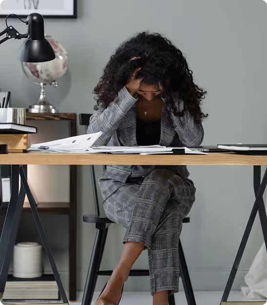 Femme assise à un bureau, tête dans les mains, semblant stressée devant des documents.