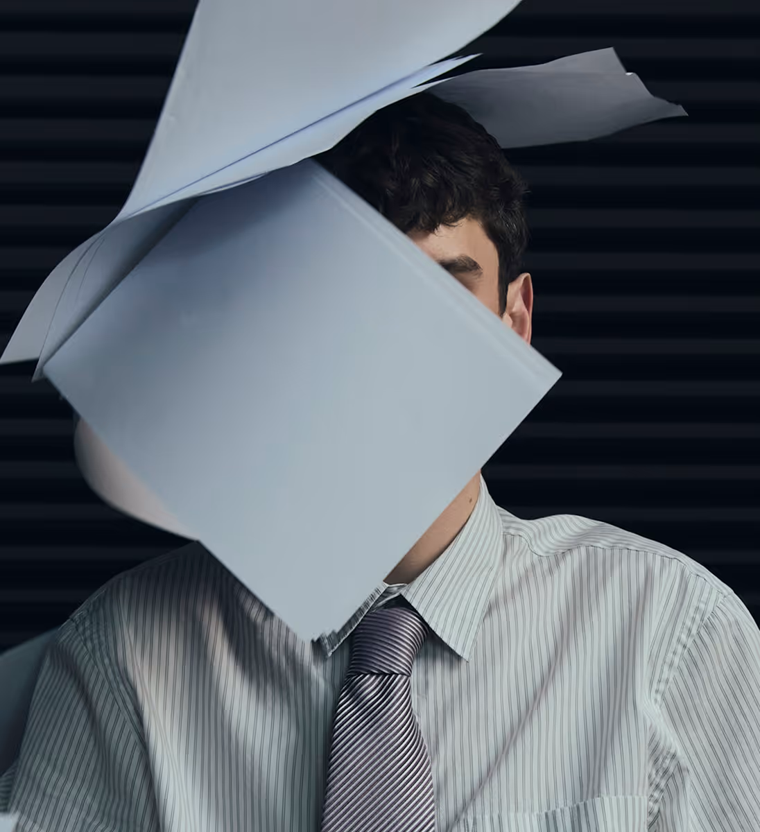Un homme en chemise rayée et cravate dont le visage est caché par des feuilles volantes.