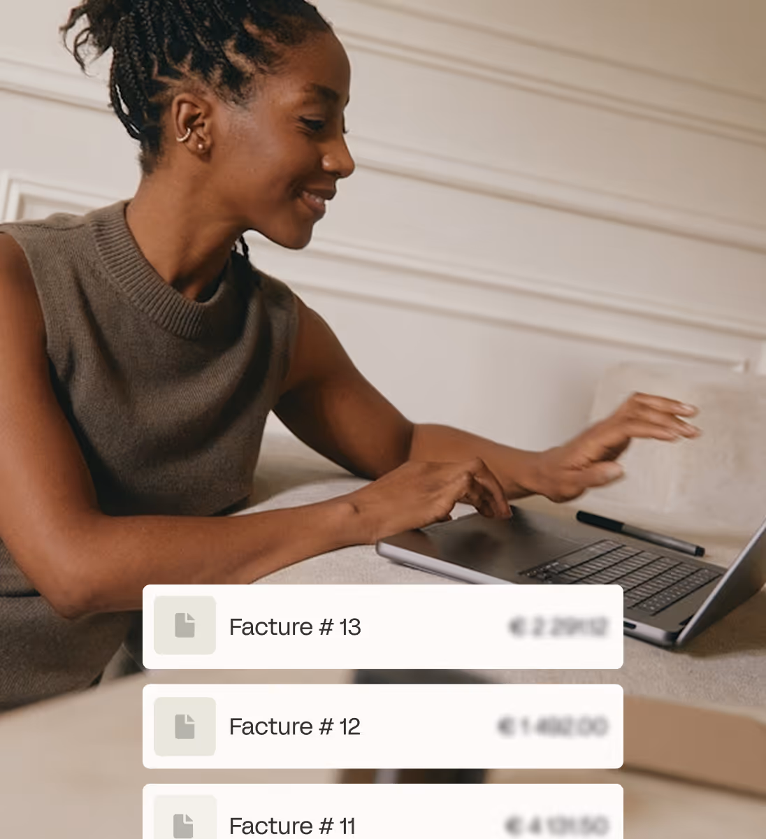 Jeune femme souriante utilisant un ordinateur portable sur un canapé avec des factures à l'écran.