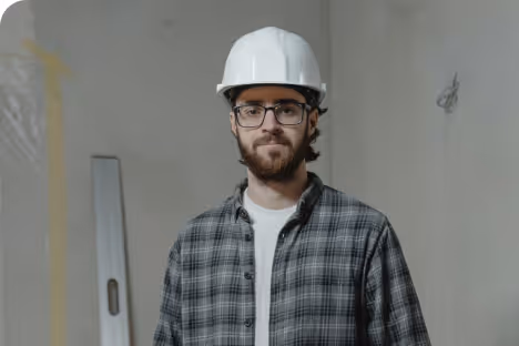 Homme portant un casque blanc et une chemise à carreaux dans un chantier intérieur.