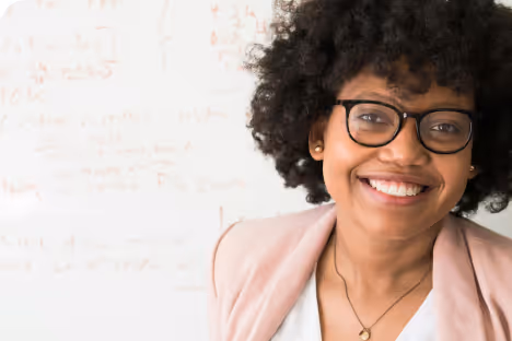 Jeune femme souriante avec lunettes et cheveux bouclés portant un blazer rose pâle.