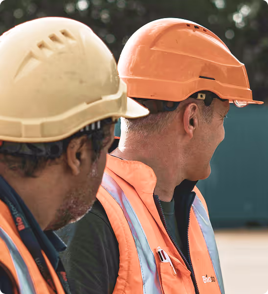 Deux ouvriers en casques de chantier et gilets réfléchissants, regardant vers la droite.