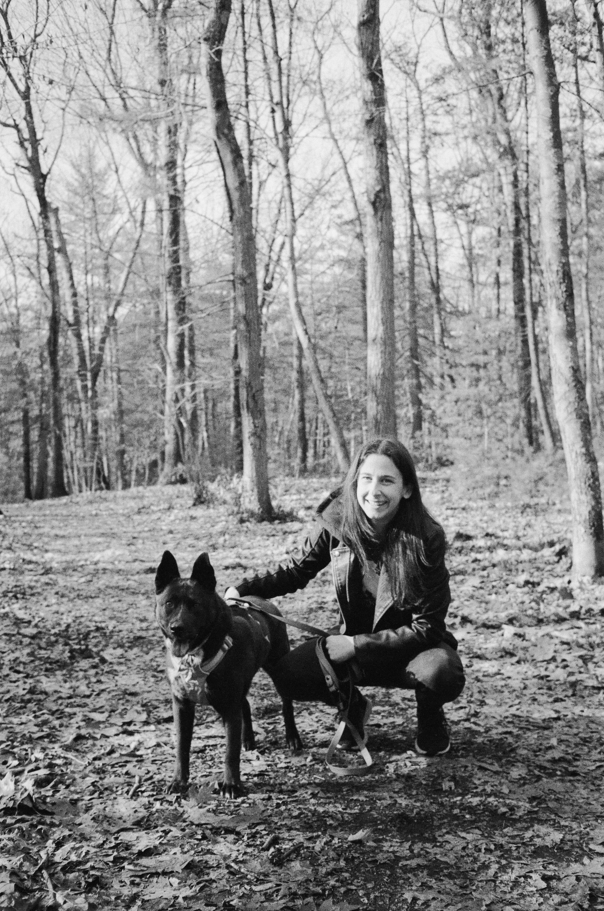 Sophie in the woods crouched down next to her dog Meesha both smiling at the camera