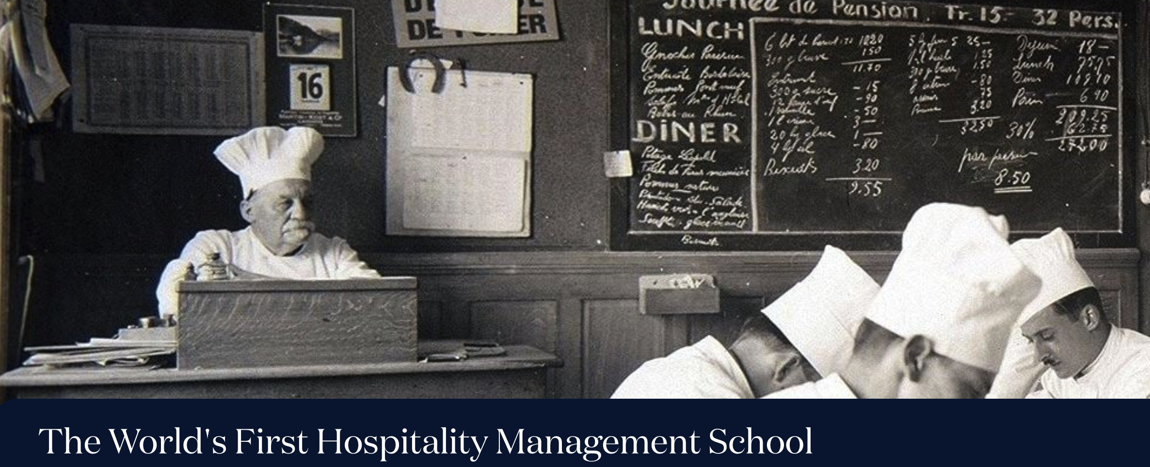 Chefs in white uniforms working under an older chef with a chalkboard menu behind them.