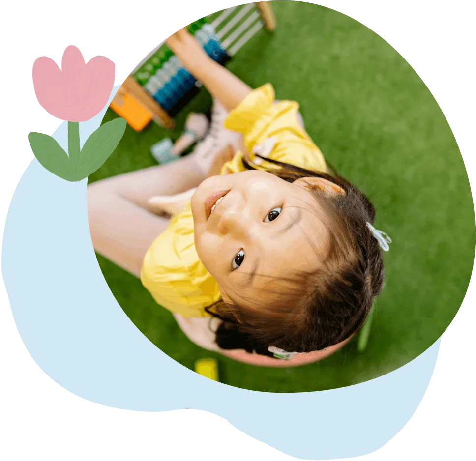 Smiling young girl in a yellow dress looking up while playing on green grass.