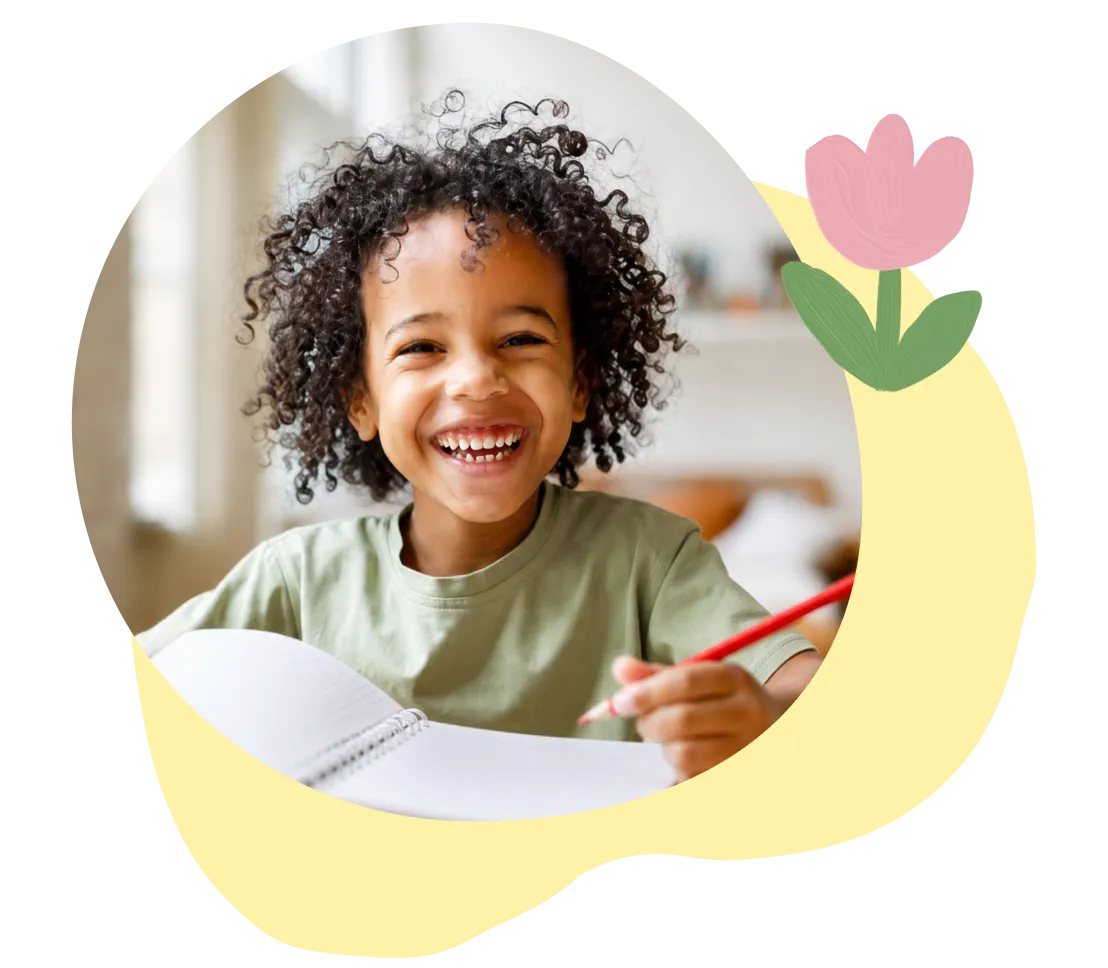 Smiling child with curly hair holding a red pencil and writing in a notebook at home.
