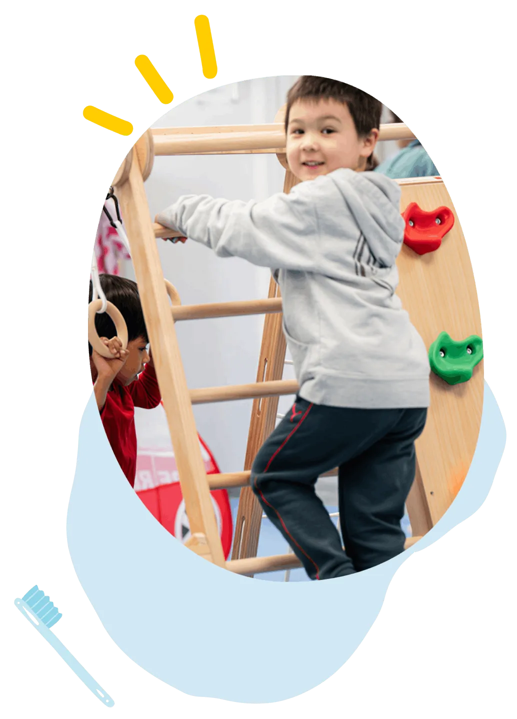 Two children playing on indoor wooden climbing equipment with rings and colorful rock holds.
