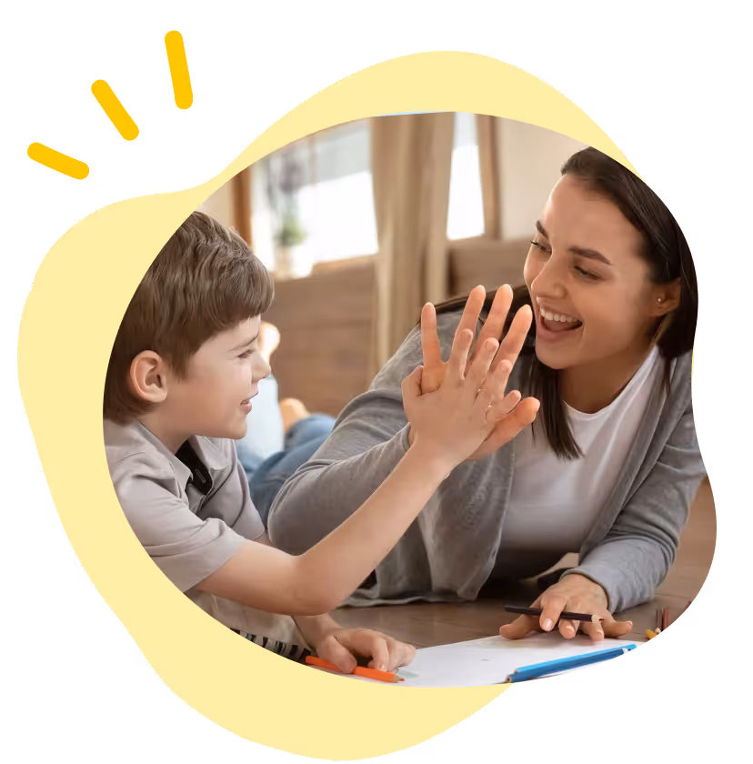 Smiling woman and boy giving a high five while drawing together on the floor at home.