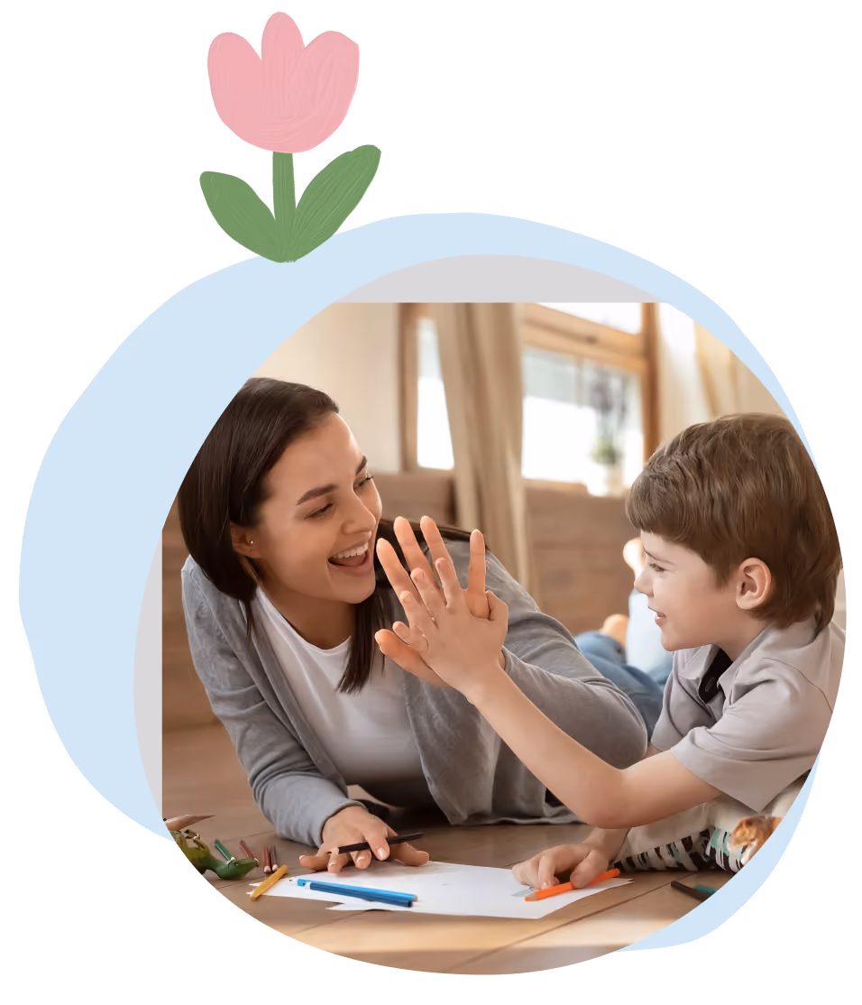 Woman and young boy laying on floor smiling and giving each other a high-five while drawing.