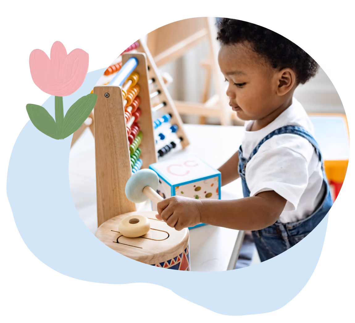 Toddler playing with a wooden drum and abacus on a white table indoors.
