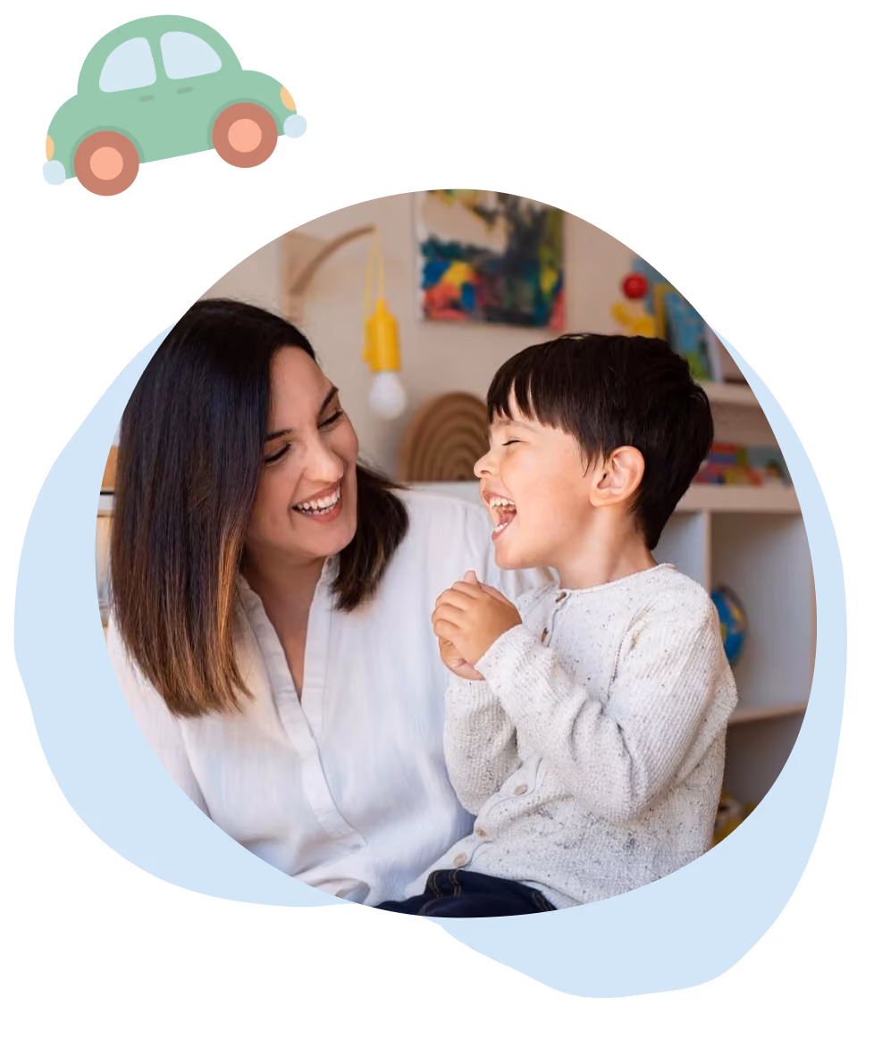 Smiling woman and young boy laughing together in a cozy room with colorful artwork and toys.