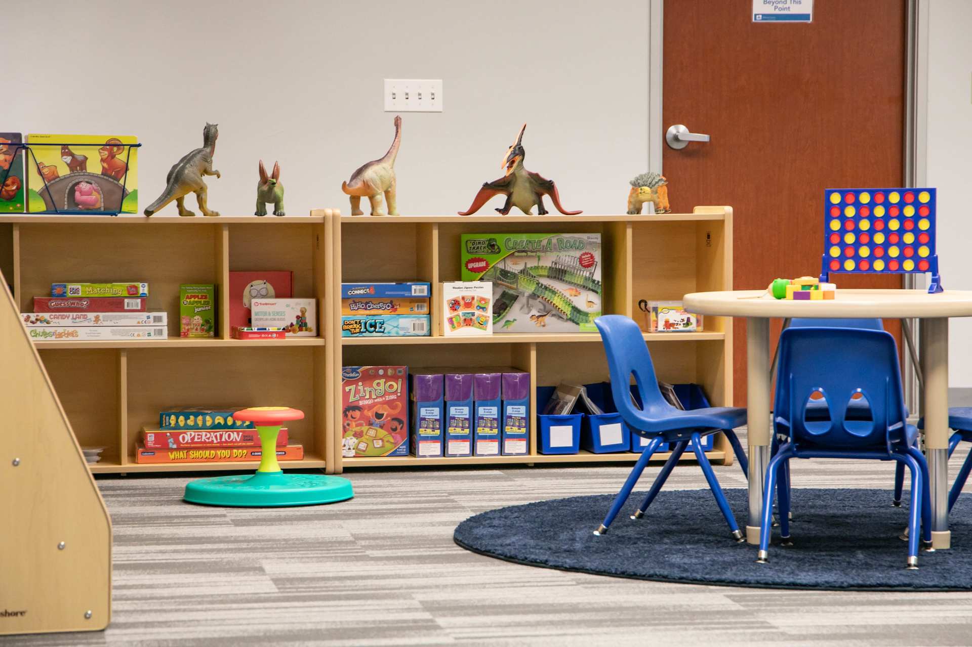 Shelf of board games and dinosaur toys next to a round table in a Behavior Frontiers ABA therapy center activity room