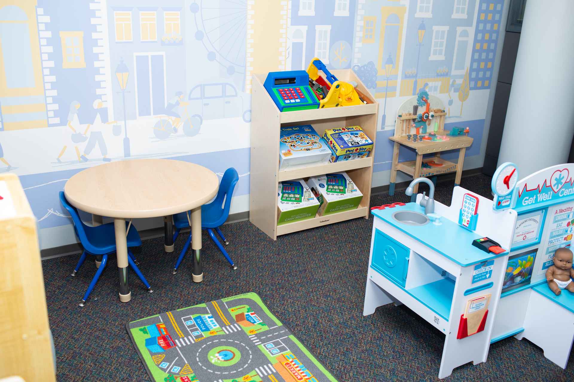 Pretend play kitchen and cash register shelf beside a city mural in an ABA clinic dramatic play room