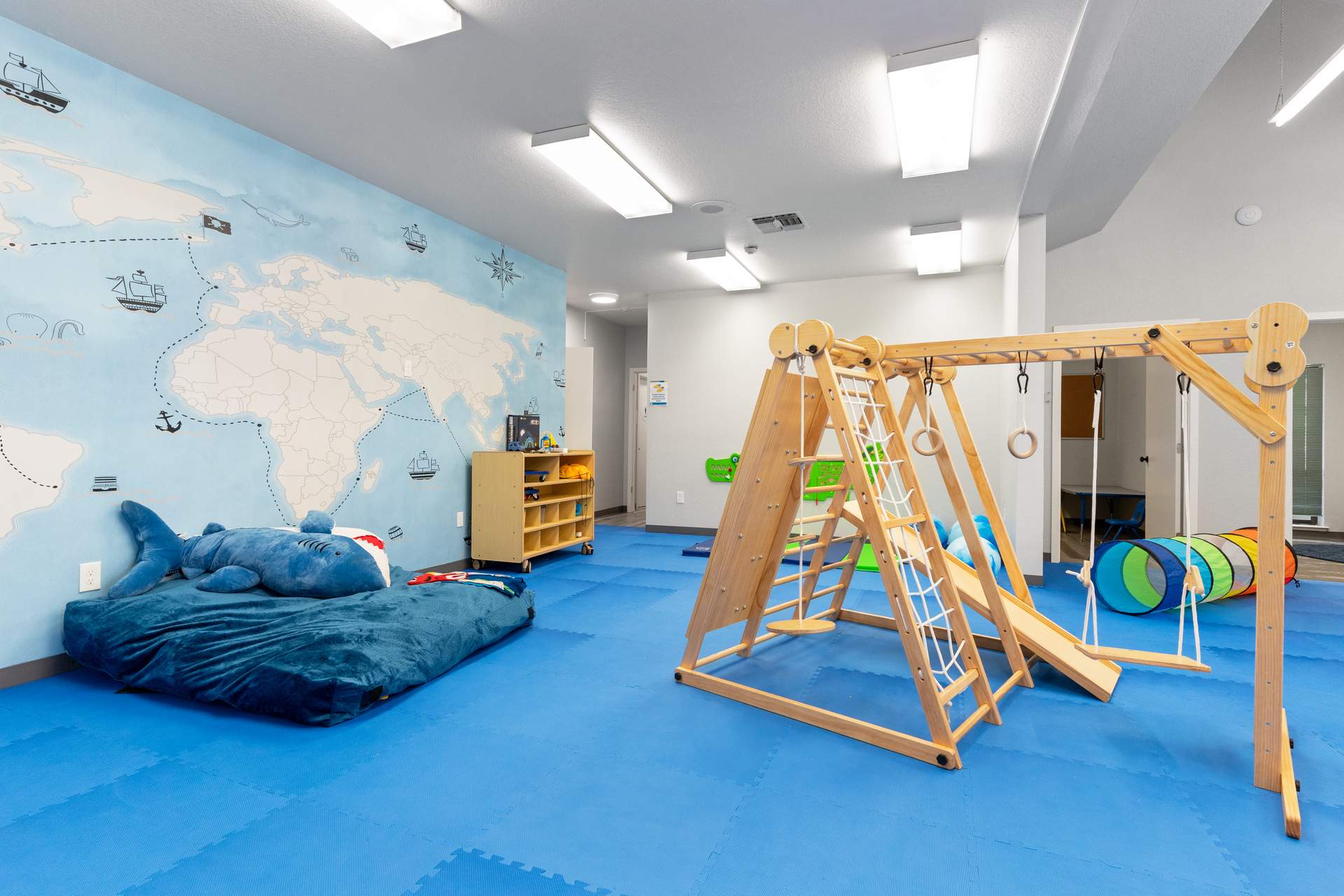 Sensory motor room with wooden climbing triangle, swing, and floor cushion in an autism ABA therapy center