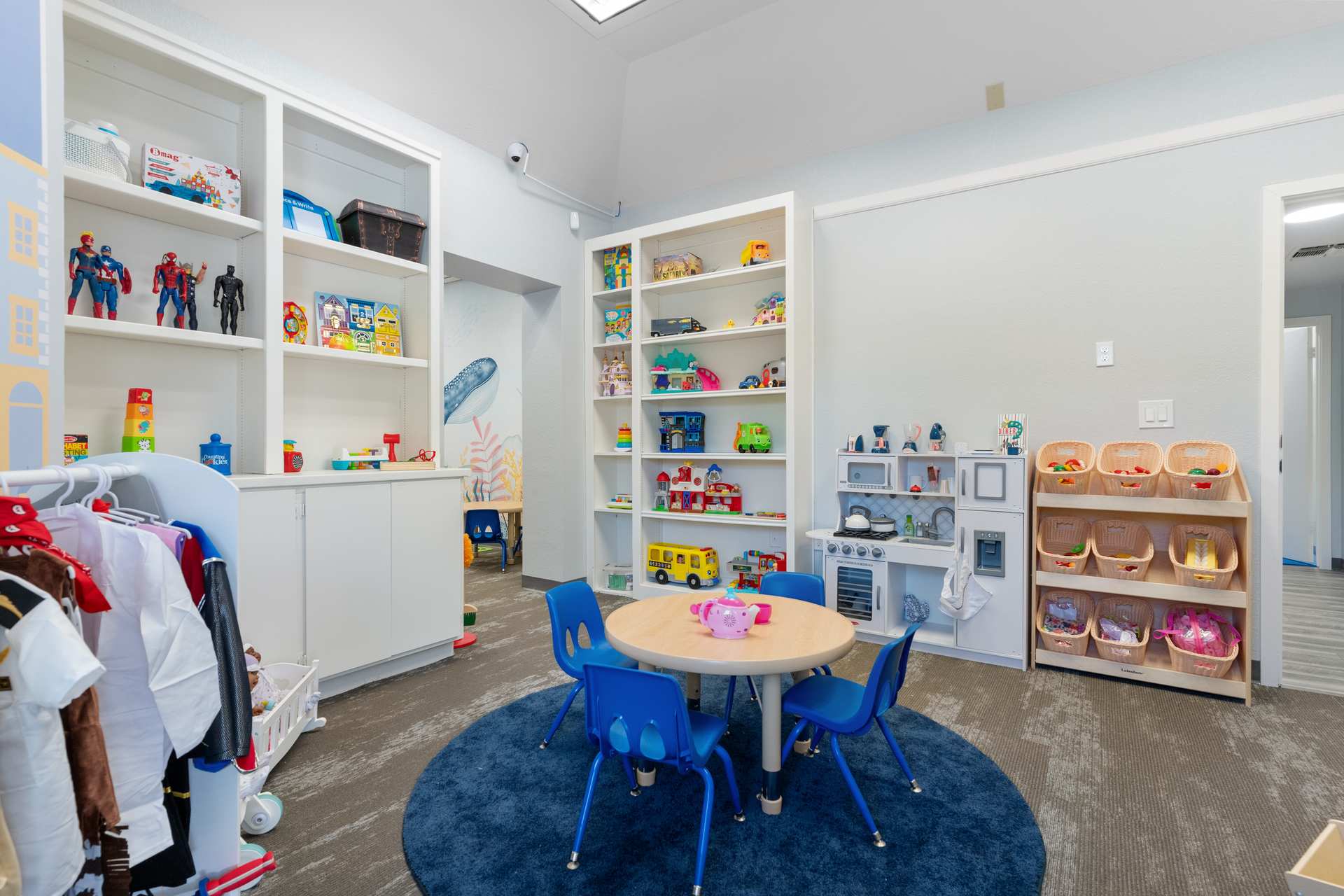 Dramatic play room with superhero figures, dollhouse toys, and dress-up costumes in an autism therapy center
