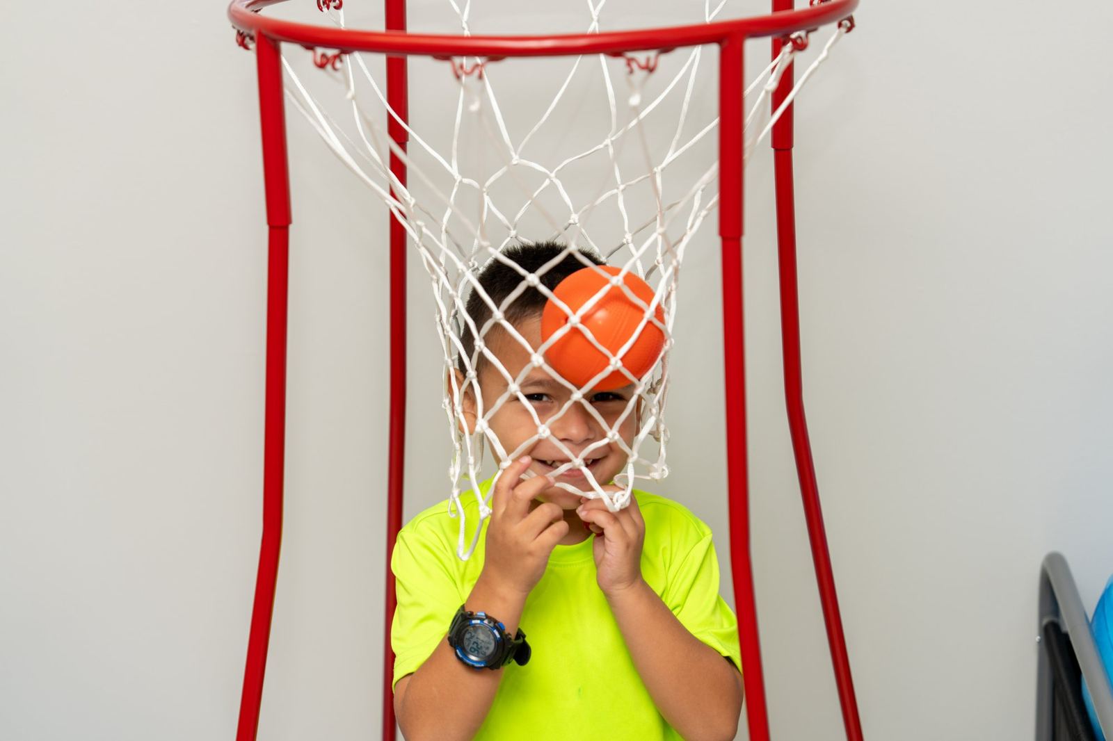 Smiling child peeking through a basketball net in the gross motor room