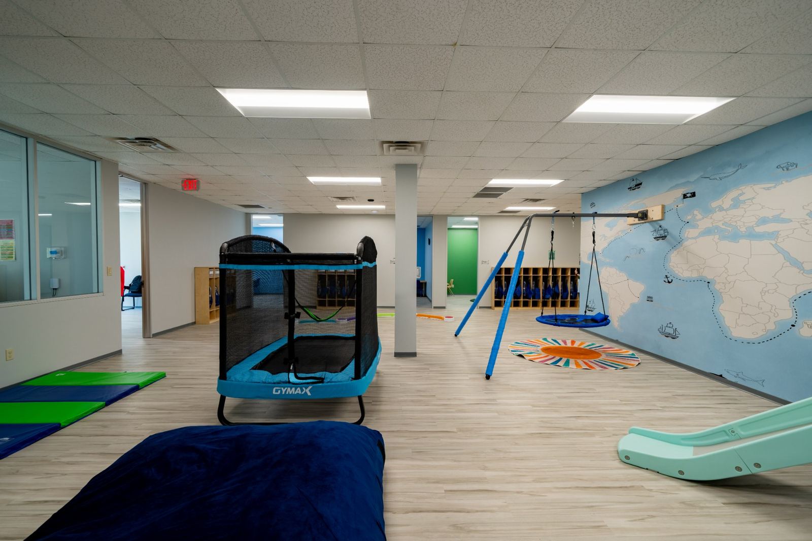 Gross motor gym room with a trampoline, platform swing, slide and world map mural