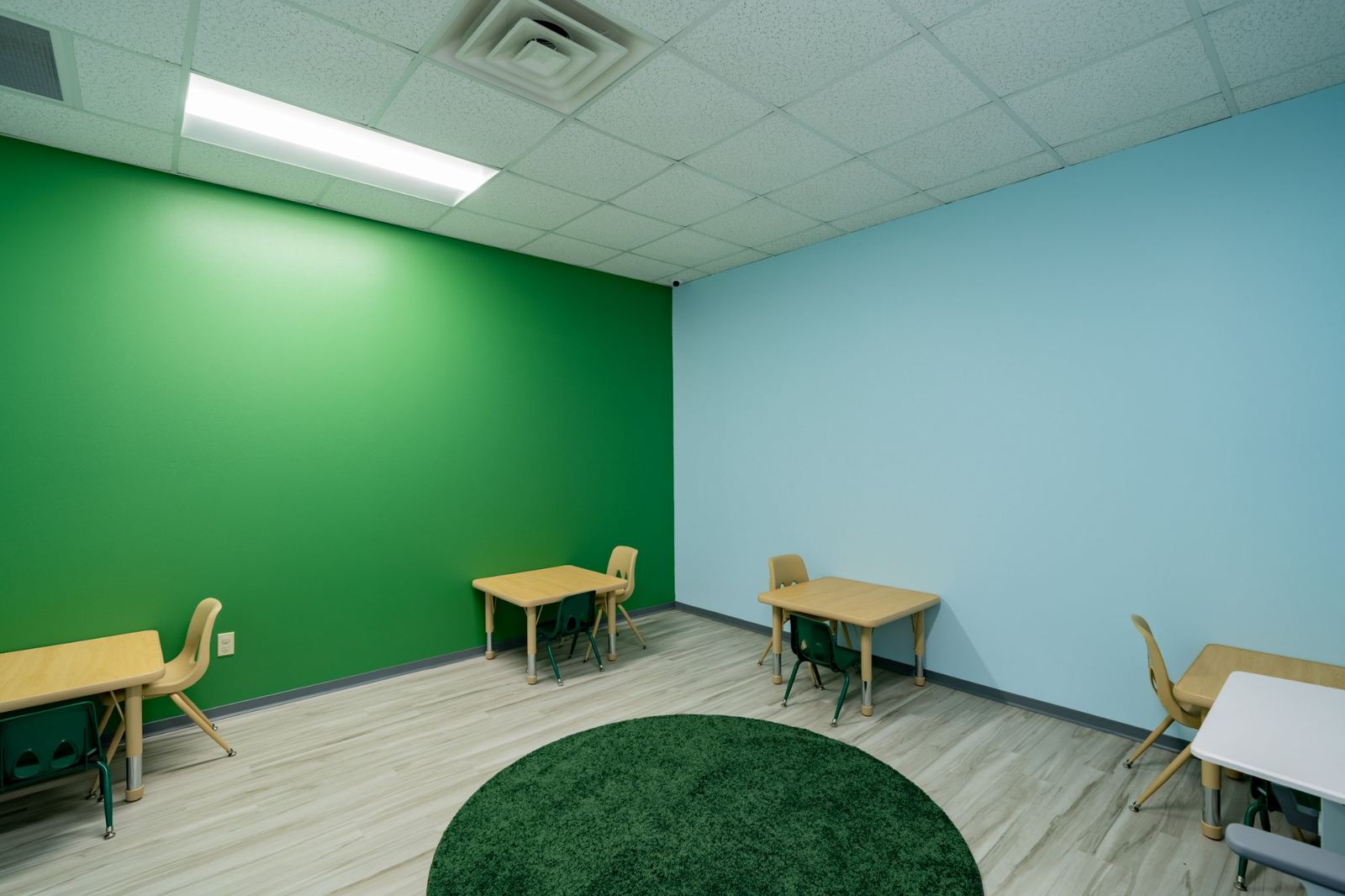 ABA therapy room with a green accent wall, small direct therapy tables and a round green rug