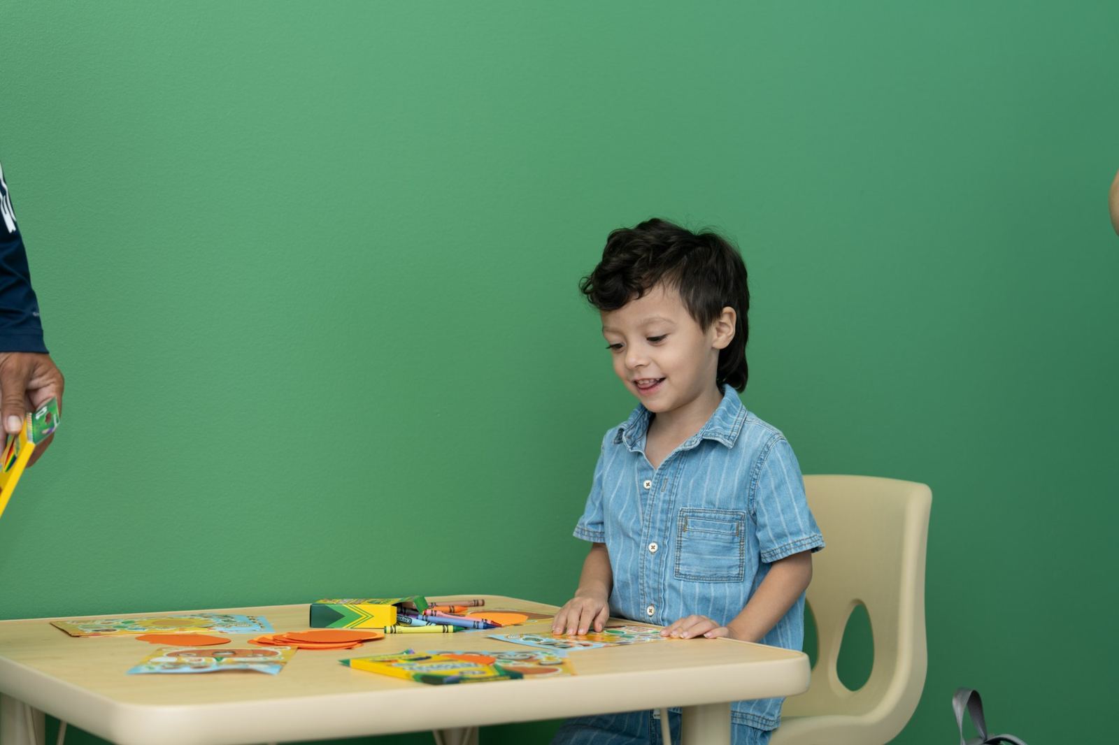 Smiling child coloring with crayons at a small therapy table