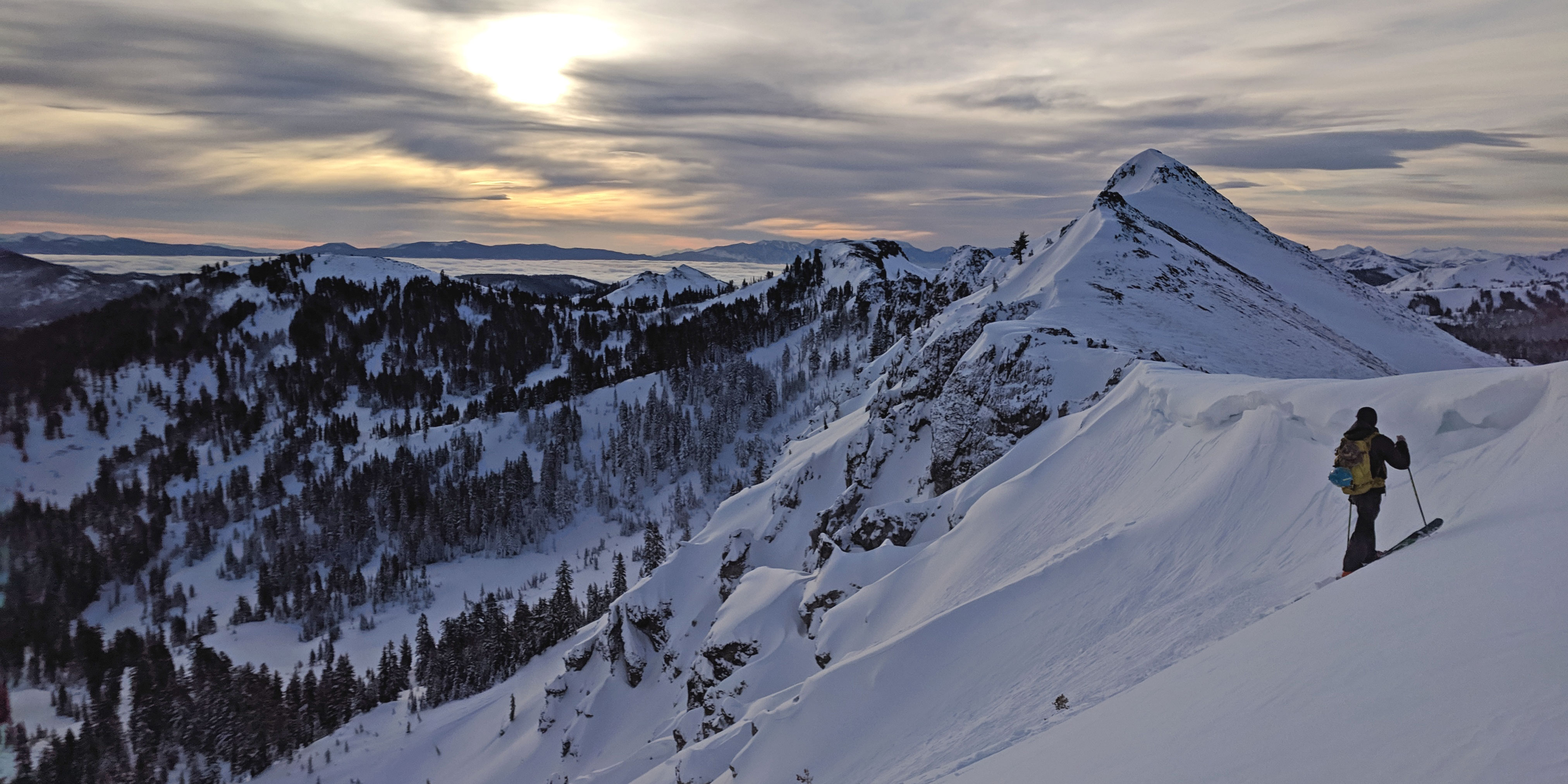 Skier looking over snowy mountain ridges towards sunrise