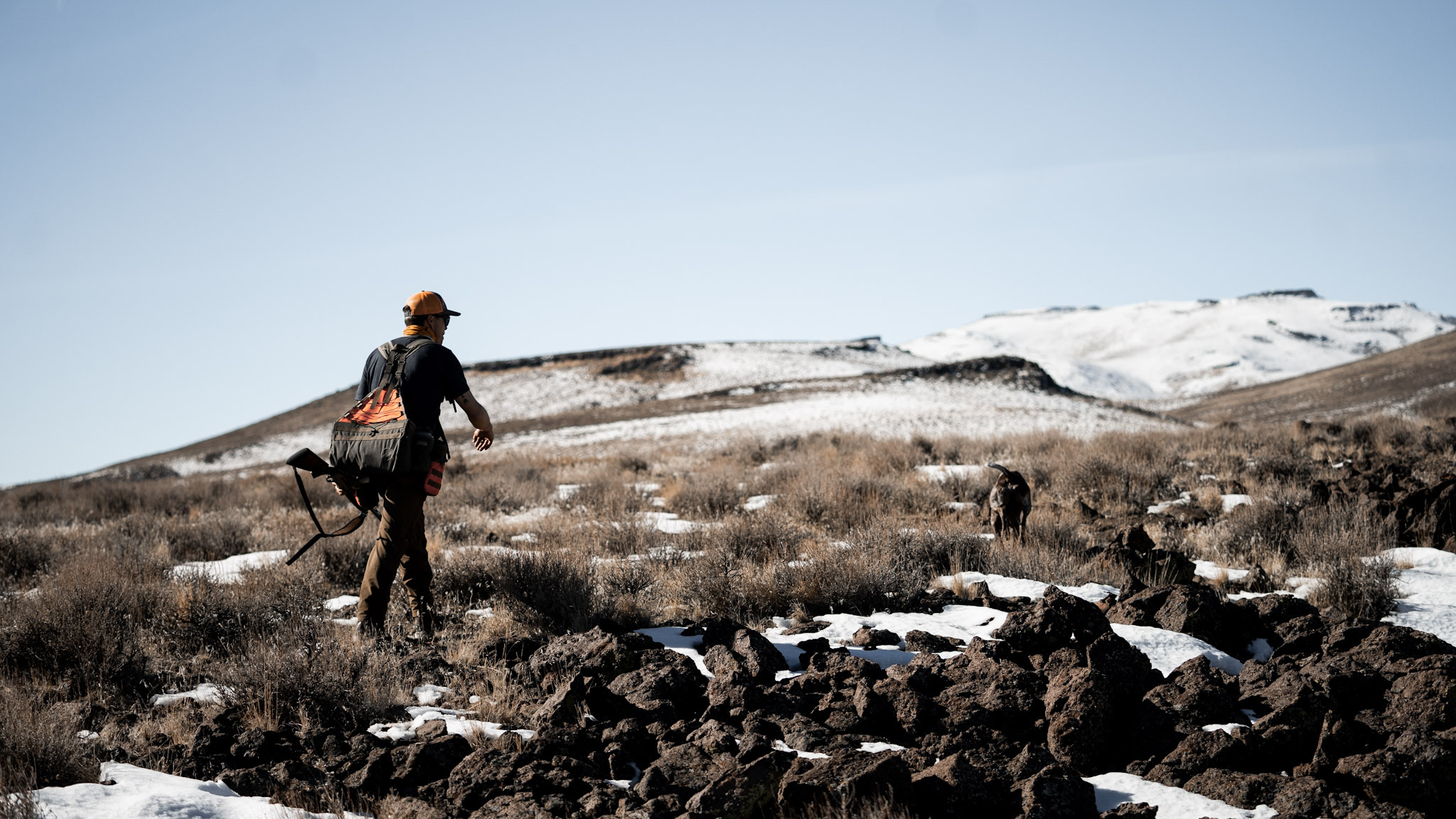 Hunter walking partially snow covered terrain