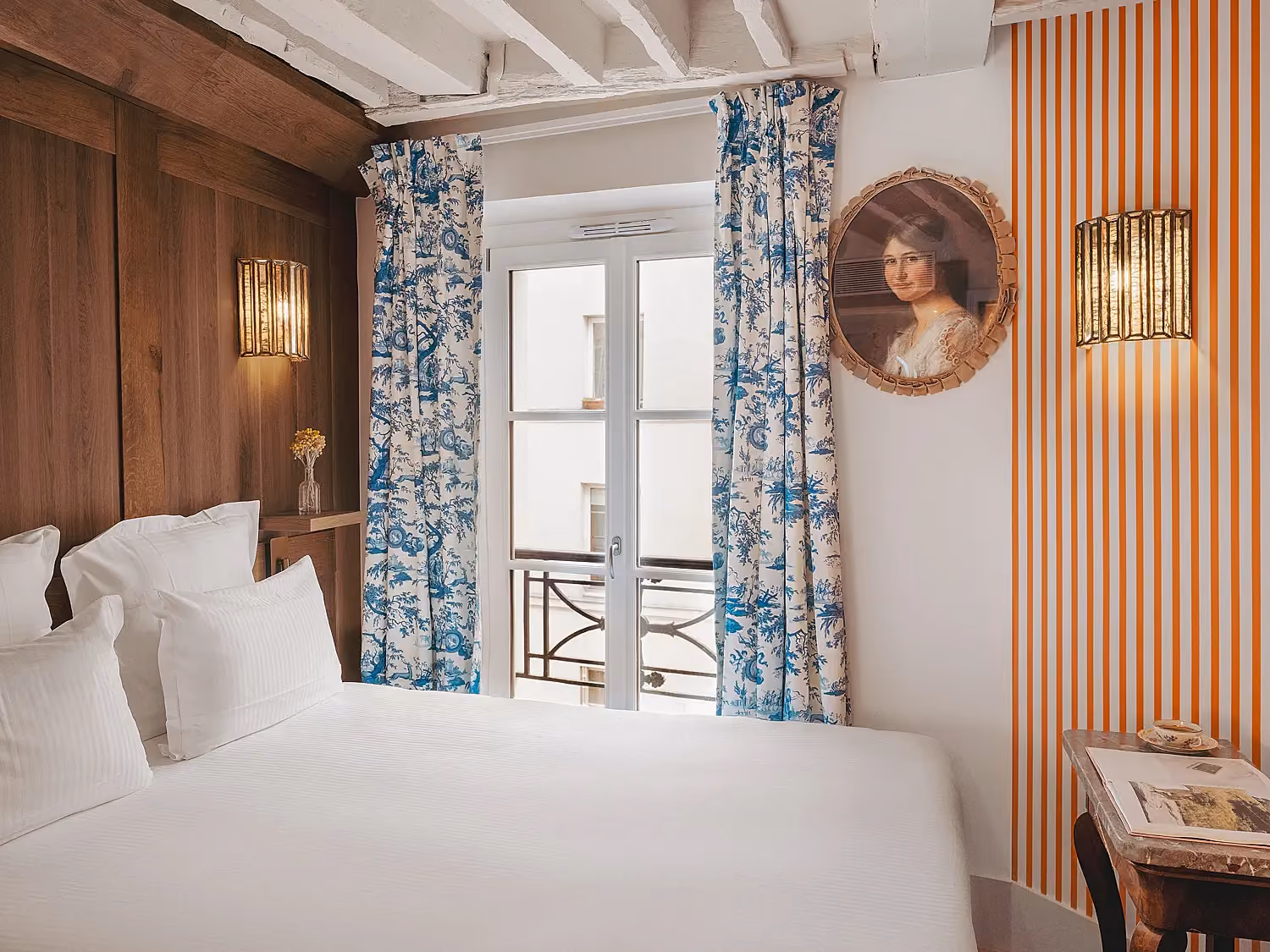 Une chambre d'hôtel parisienne cosy avec un lit double et des rideaux à motifs botaniques bleus.