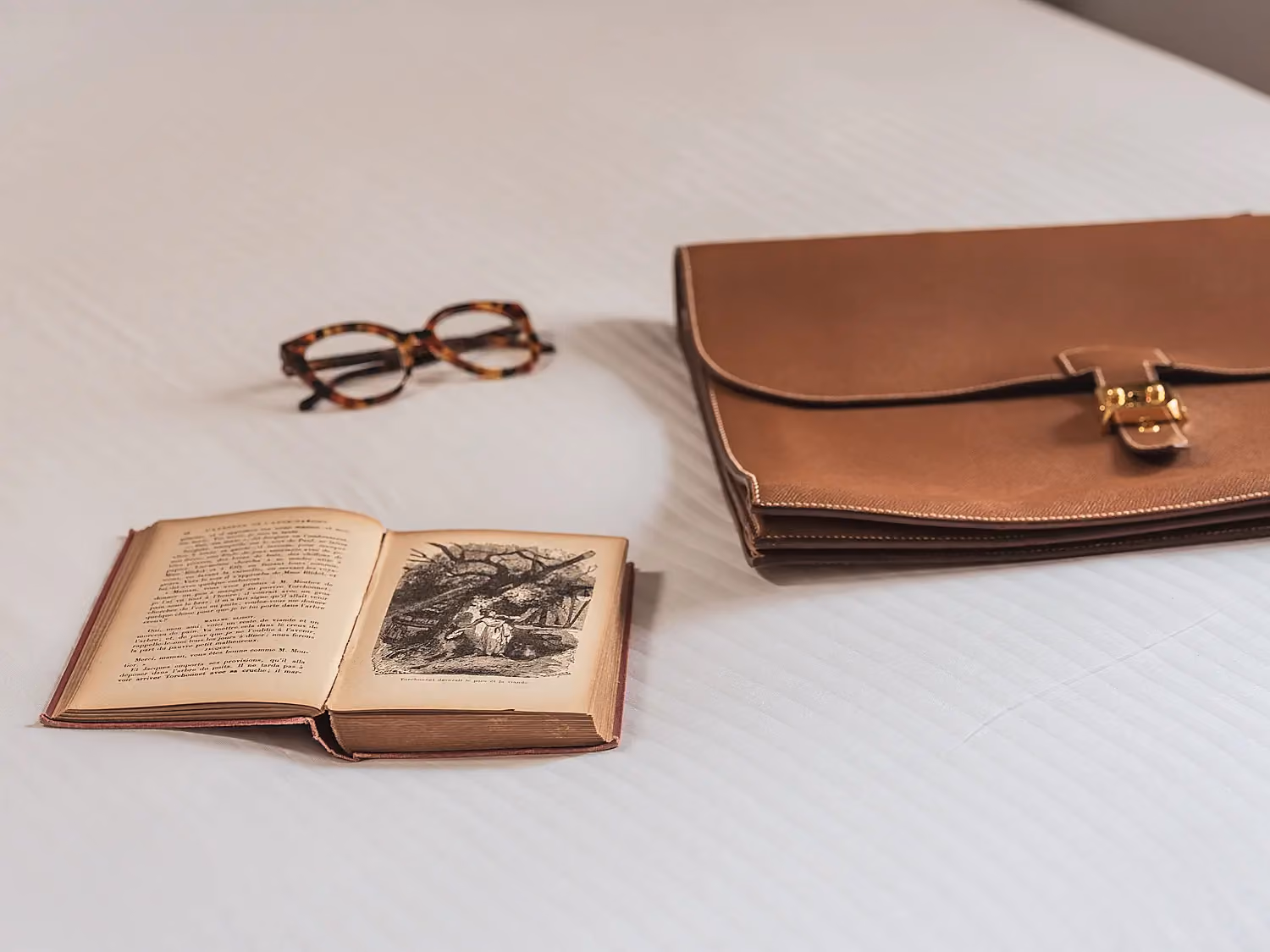 Livre ouvert avec illustration et paire de lunettes sur une table claire.