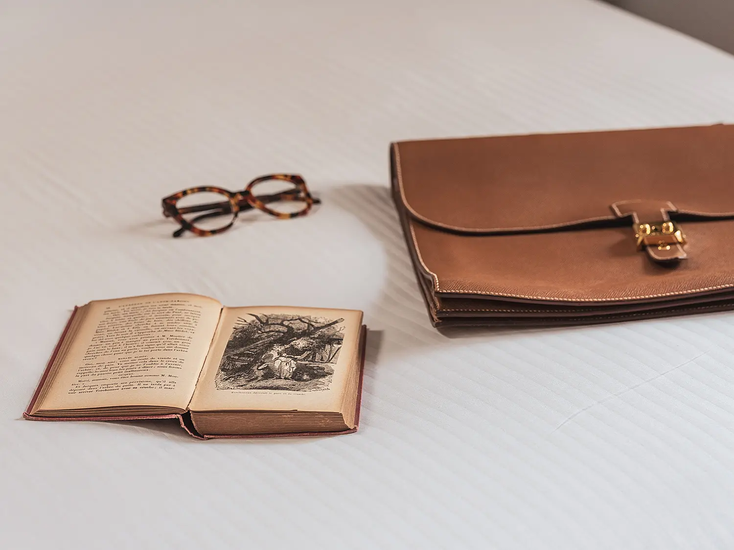 Livre ouvert avec illustration et paire de lunettes sur une table claire.