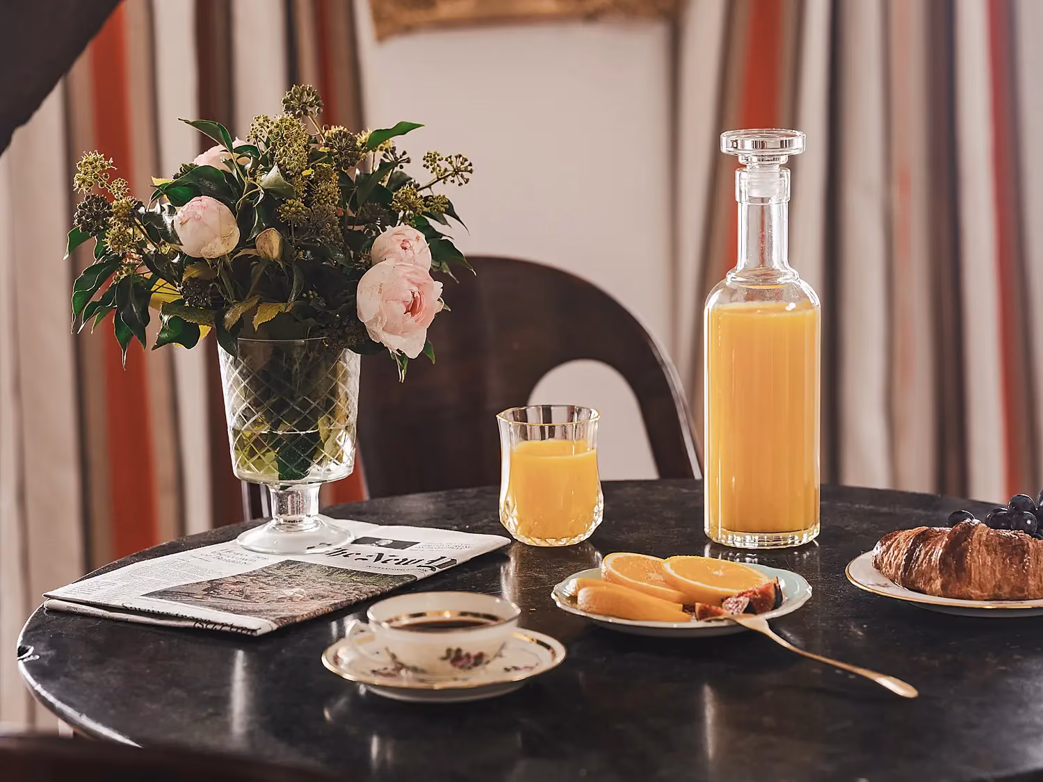 Plateau de petit-déjeuner avec jus d'orange et fleurs sur une table ronde.
