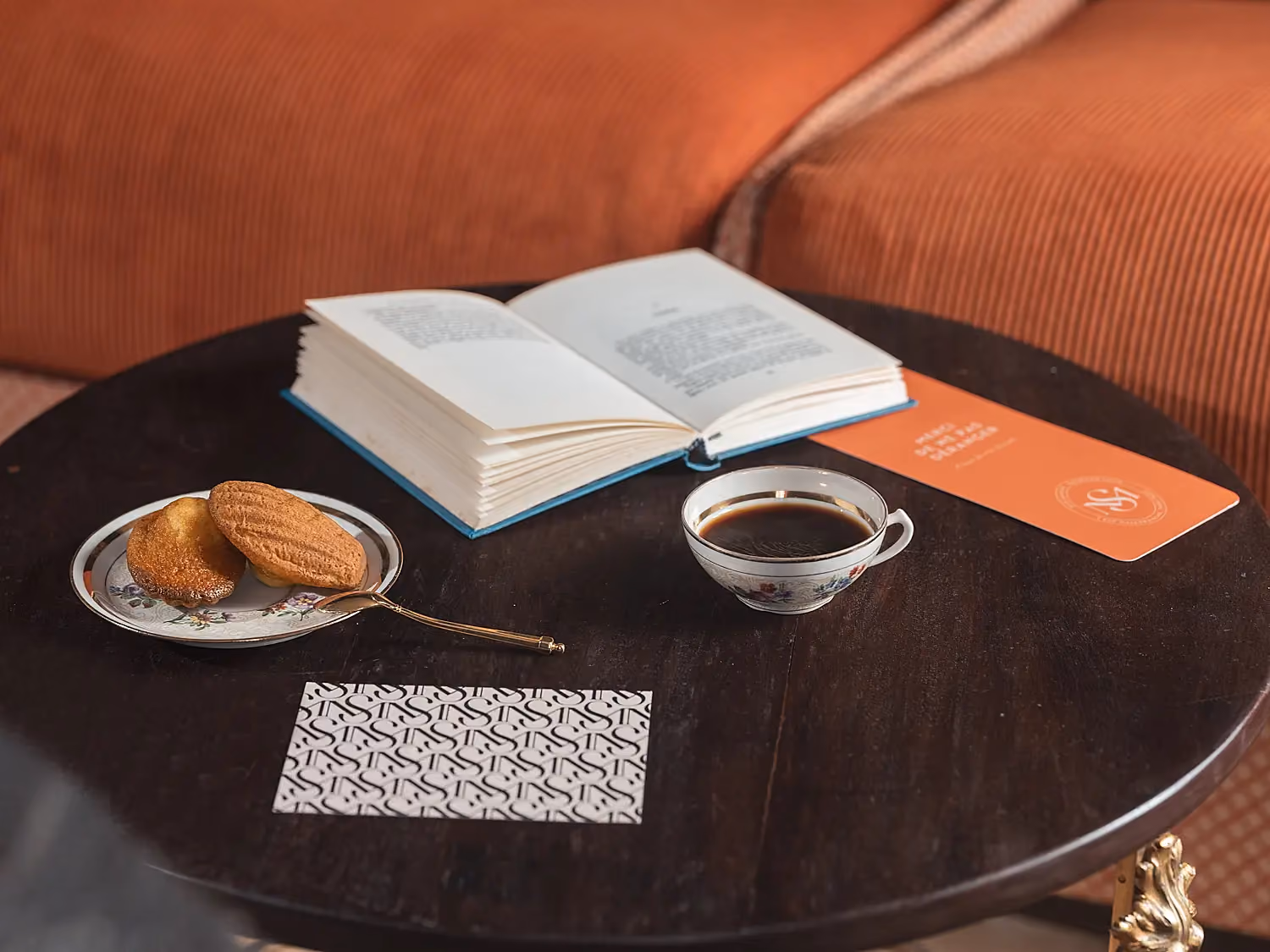 Table de salon préparée avec un livre, une tasse de café et une pâtisserie.
