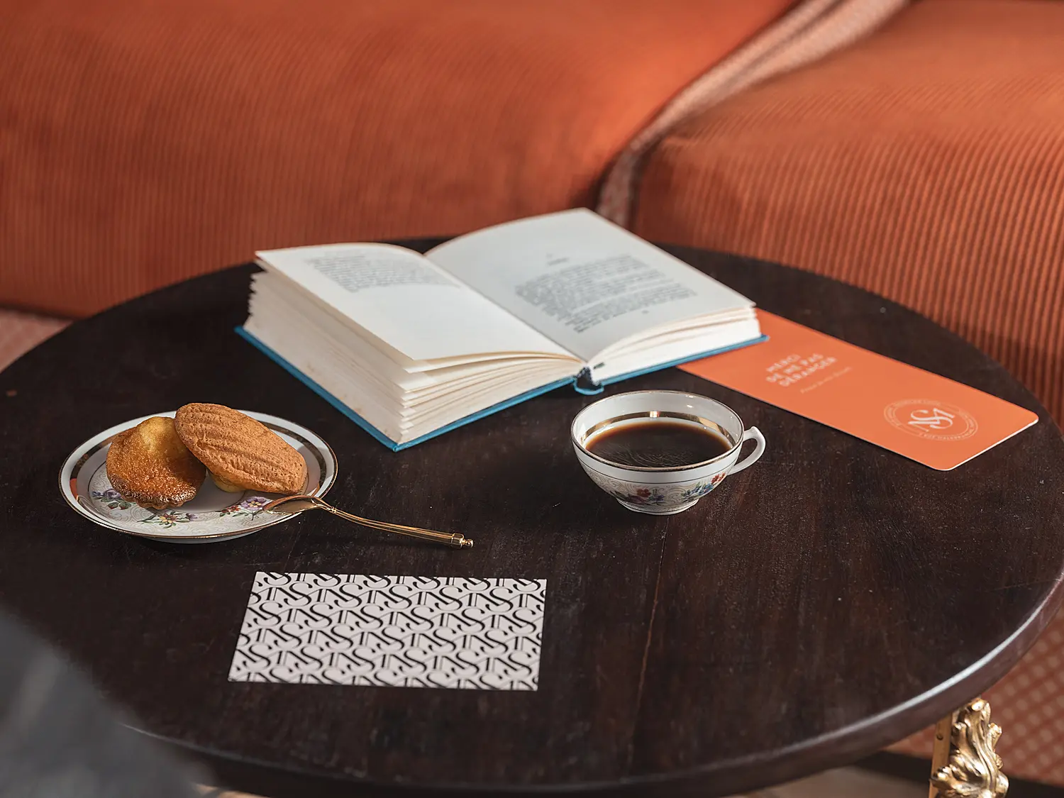 Table de salon préparée avec un livre, une tasse de café et une pâtisserie.
