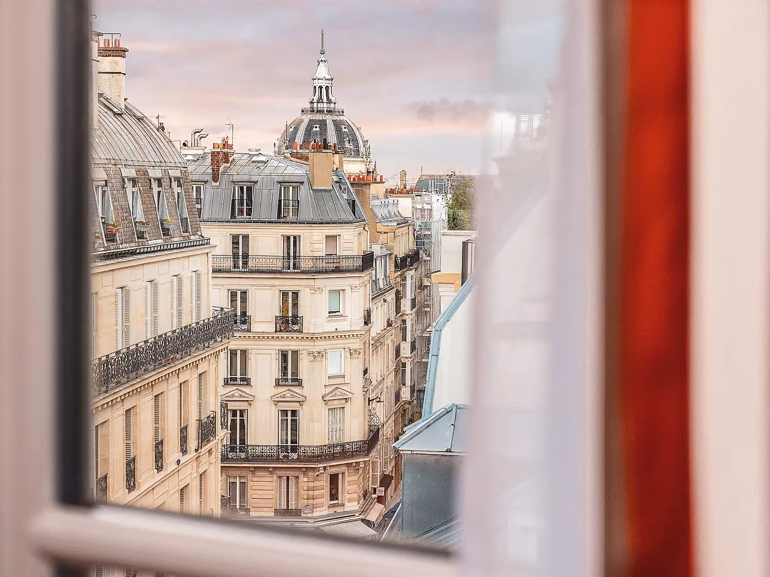 Vue plongeante sur les immeubles haussmanniens à travers une fenêtre.