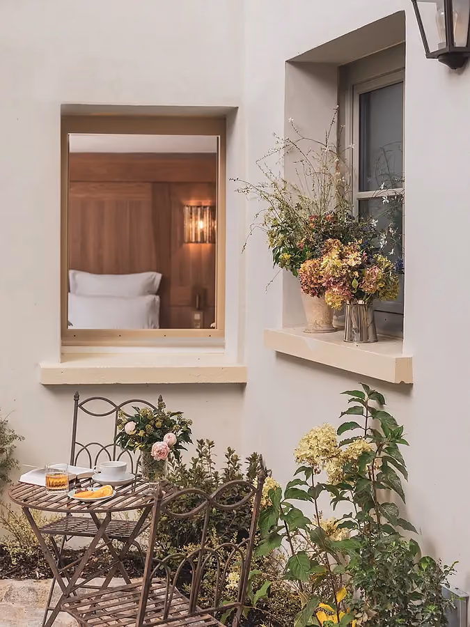 Terrasse fleurie devant une fenêtre ouverte donnant sur un intérieur.