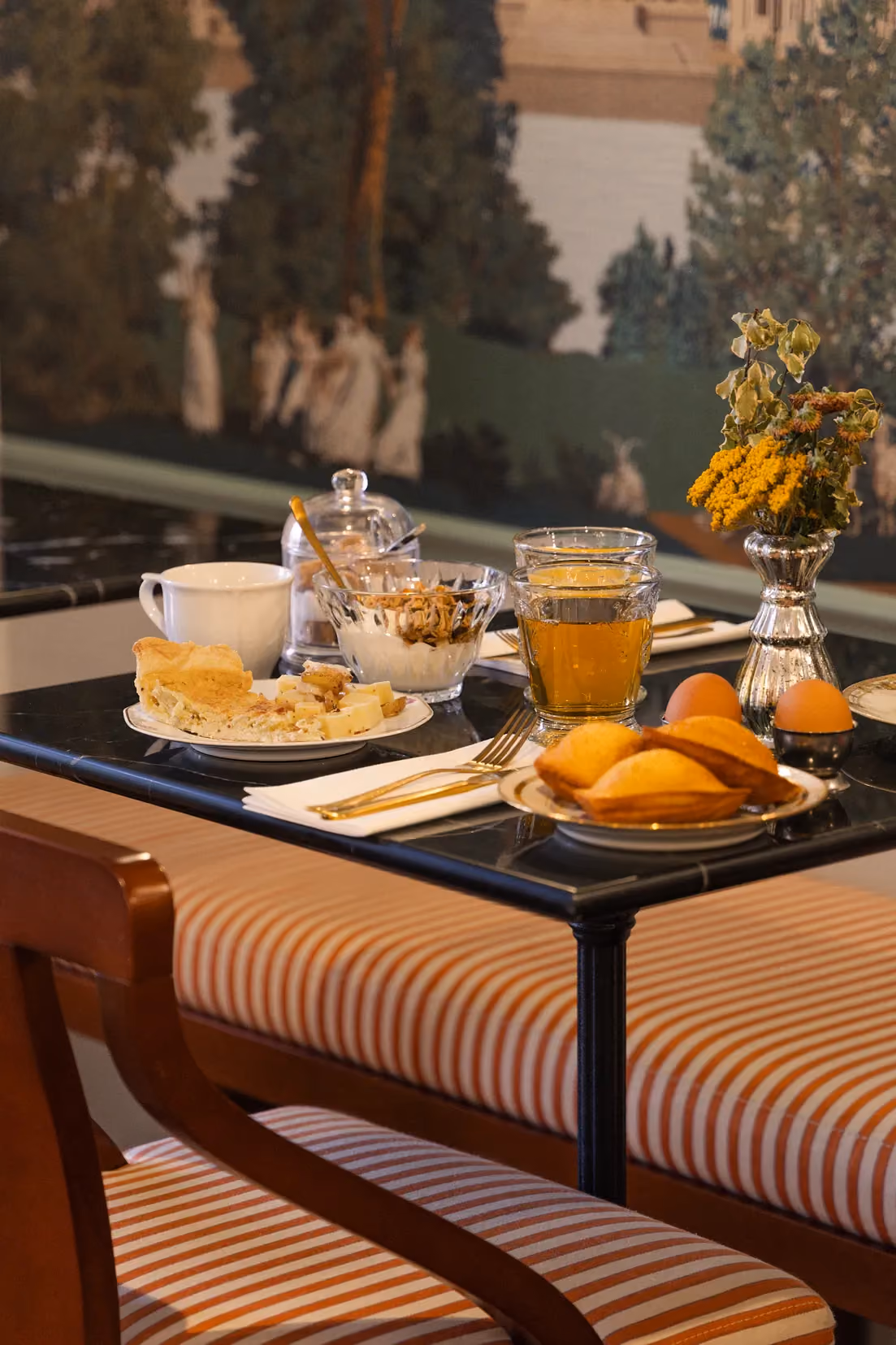 Table de petit-déjeuner élégamment préparée devant une fenêtre, avec des viennoiseries et des jus de fruits pour un repas matinal.