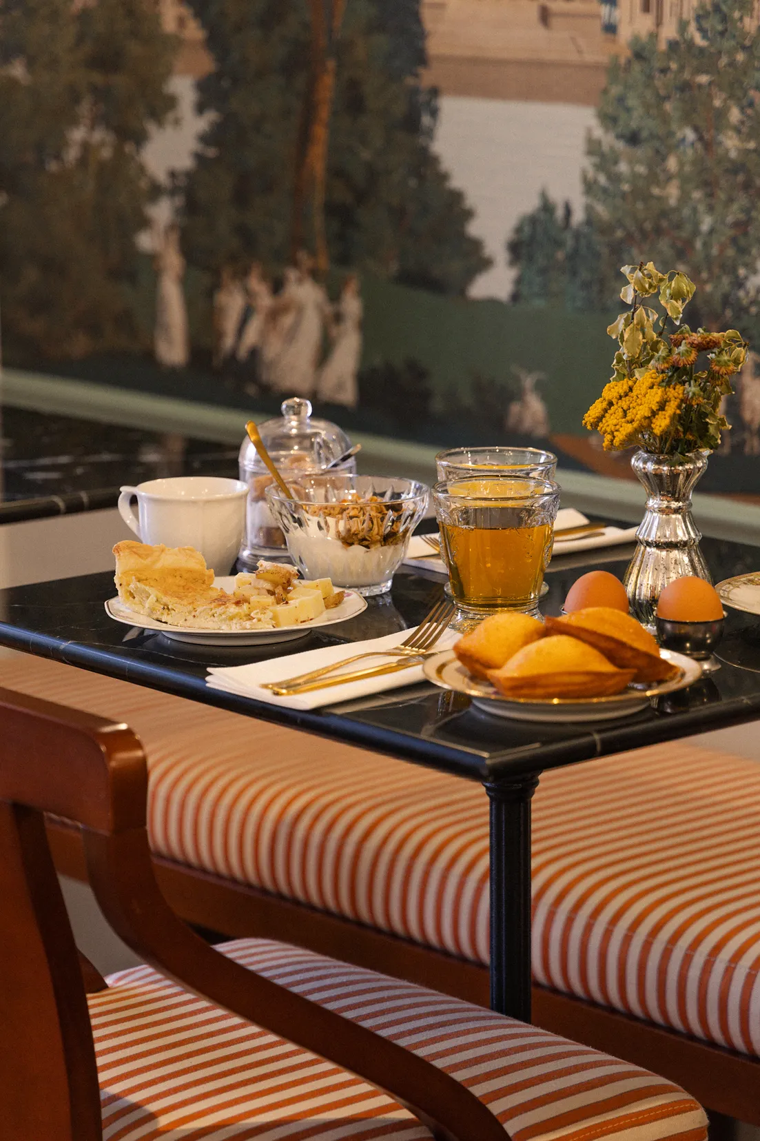 An elegantly set breakfast table in front of a window, featuring pastries and fruit juices for a morning meal.