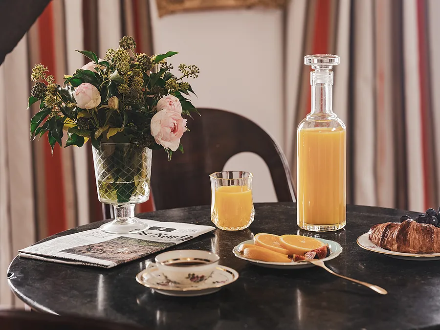 A morning arrangement on a round table featuring a carafe of juice, a bouquet of fresh flowers, and pastries.