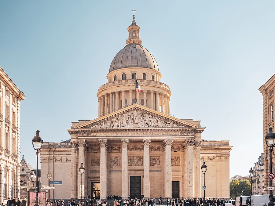 A monumental frontal view of the Panthéon in Paris under a clear blue sky.