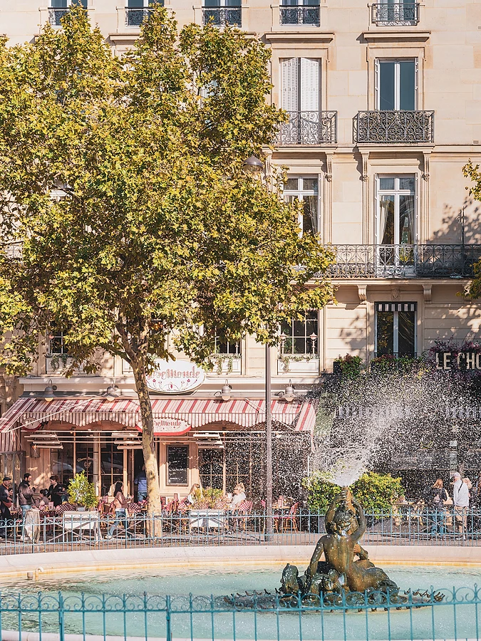 A sunny Parisian street view focusing on a traditional fountain and an old residential building.