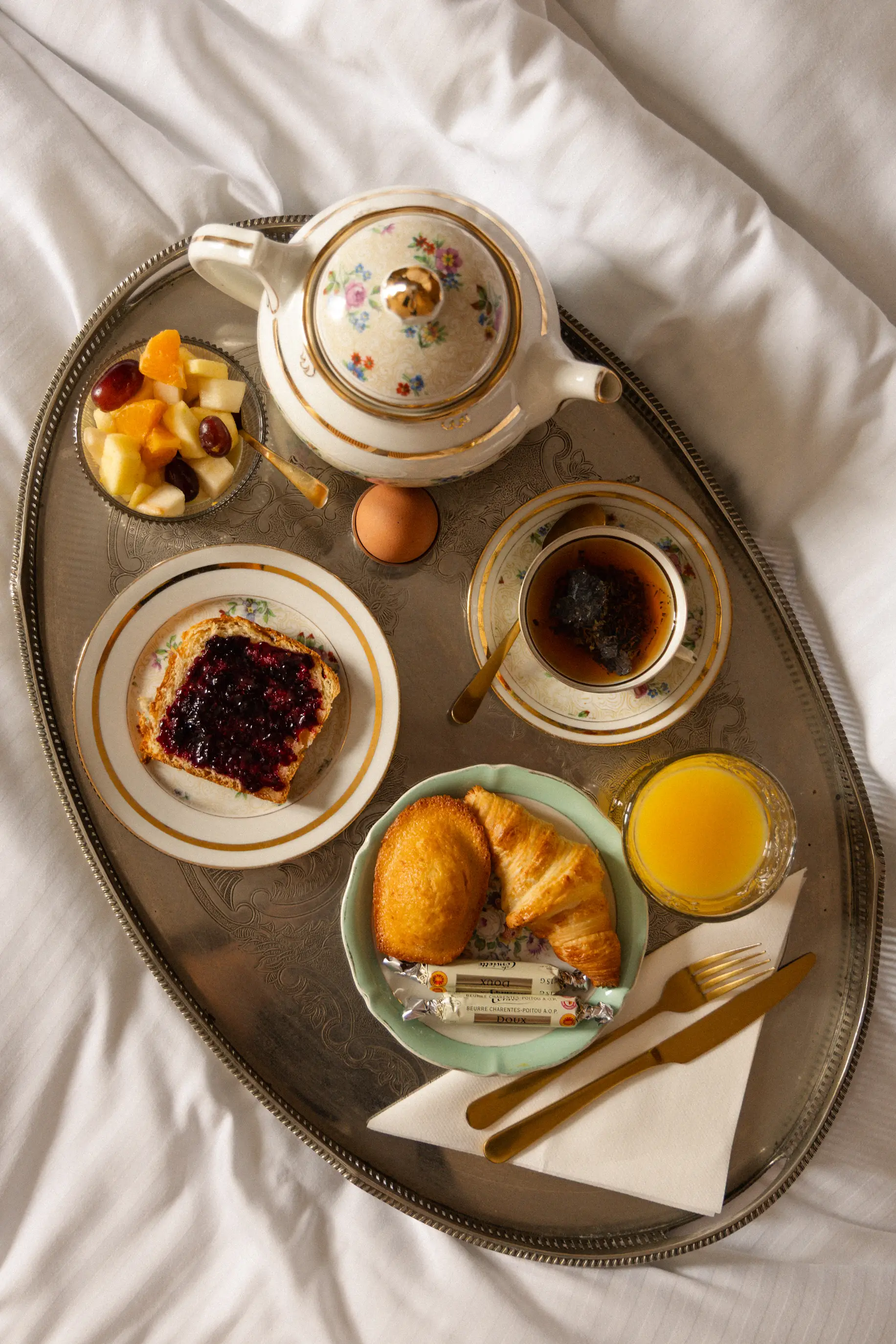 A full breakfast—consisting of tea, pastries, and fruit—served on an oval tray and placed on a bed.