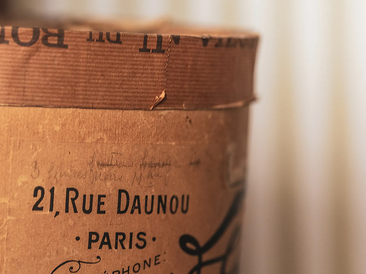 Détail d'une étiquette sur une boîte à chapeaux ancienne indiquant l'adresse Rue Daunou à Paris.