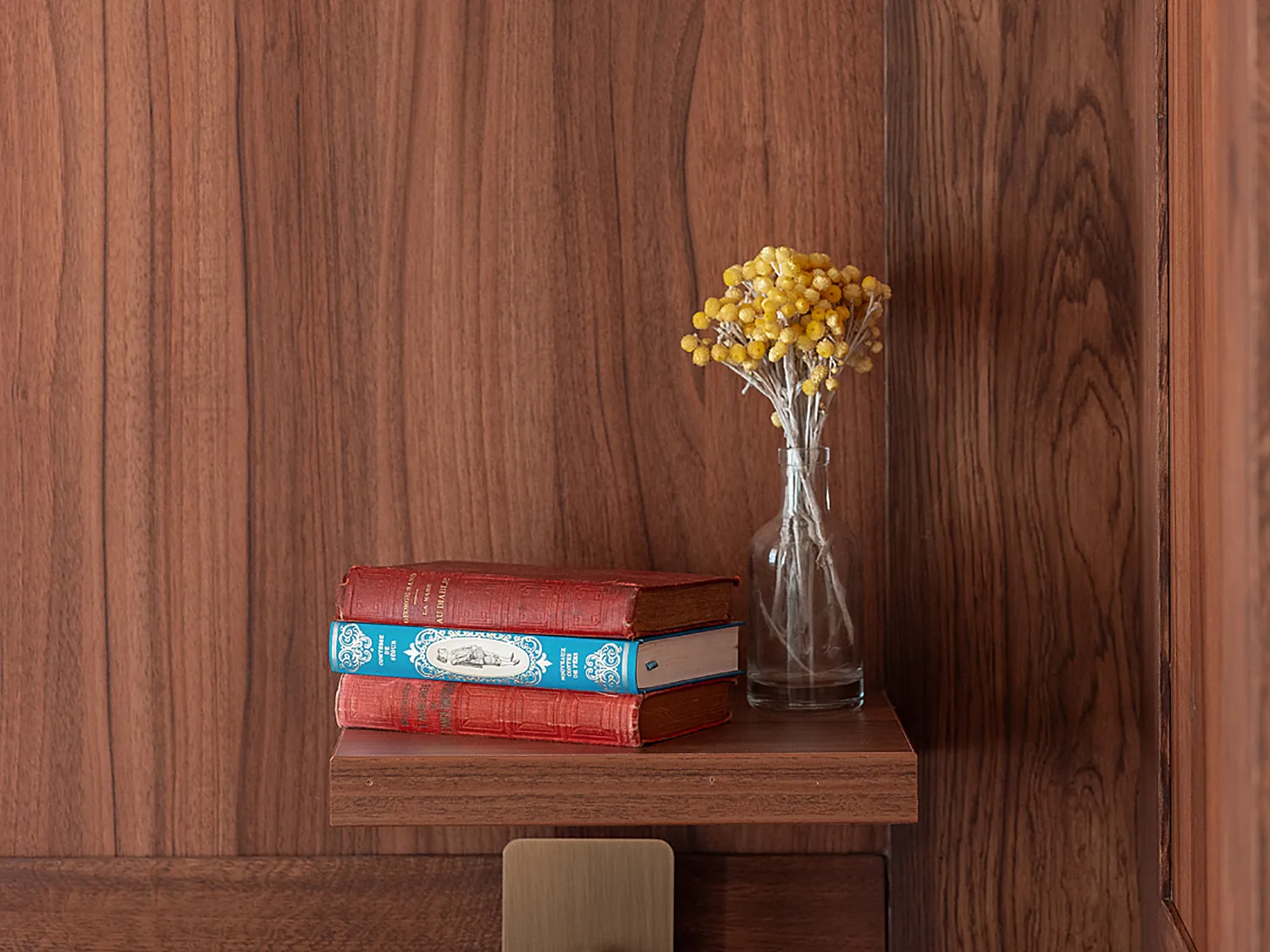Décoration minimaliste sur une étagère en bois avec fleurs jaunes et livres empilés.