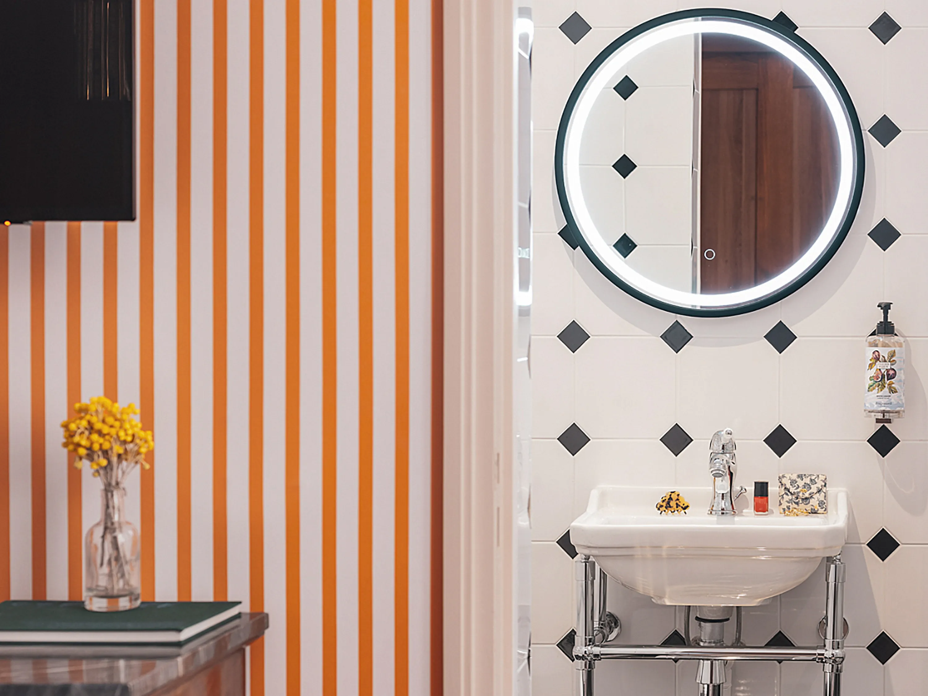 Salle de bain avec lavabo, miroir rond et papier peint rayé orange.