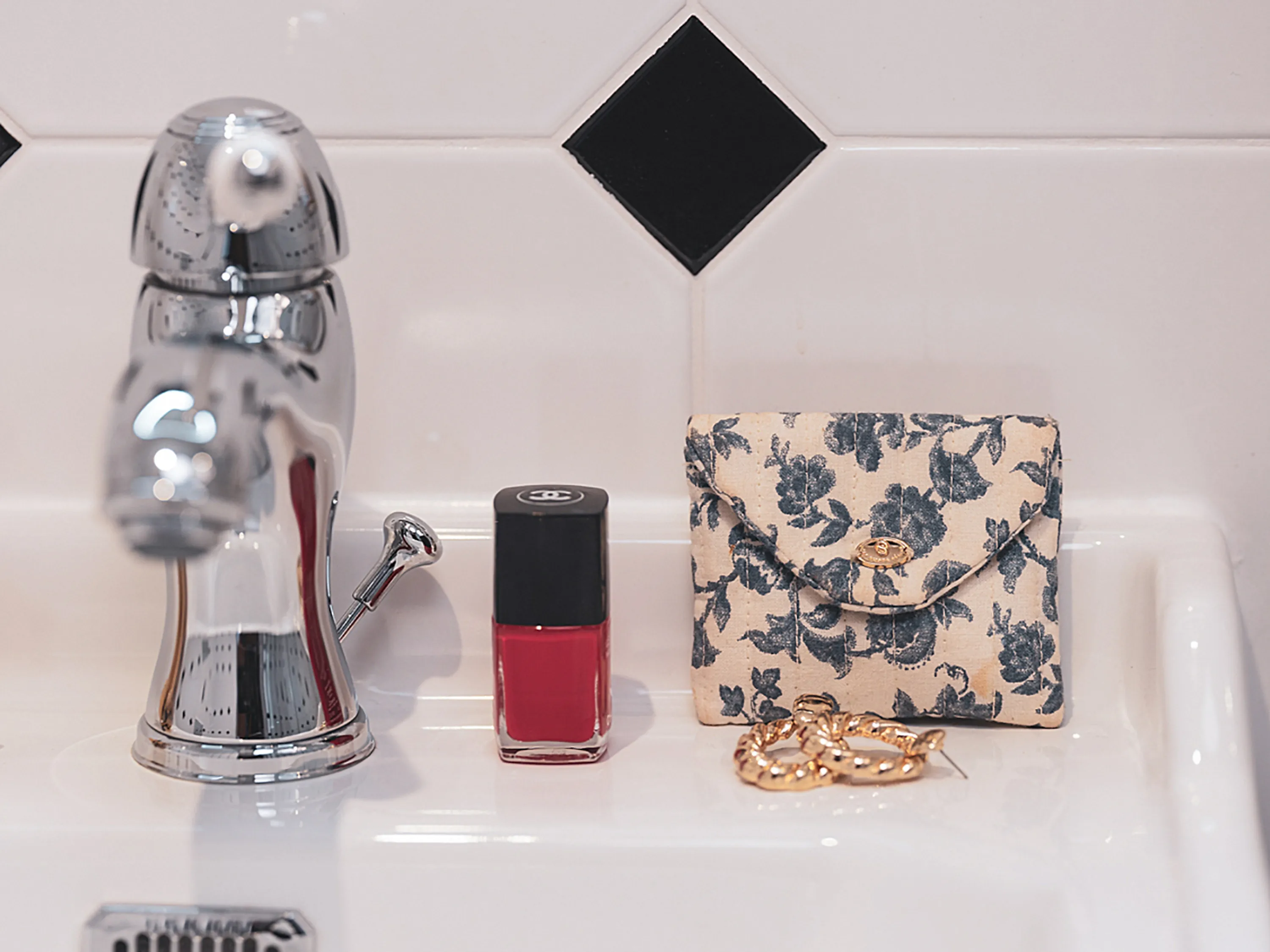 Objets de toilette, dont une pochette à fleurs et un rouge à lèvres, sur un lavabo.