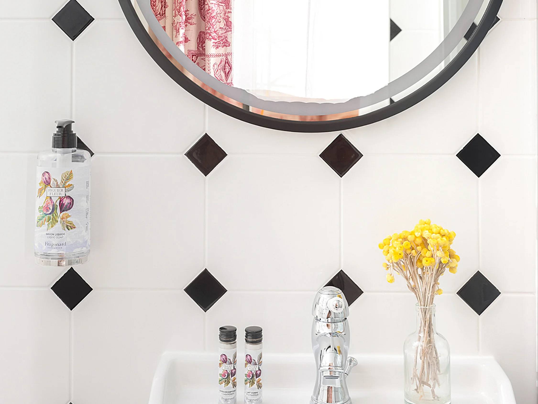 Un détail de la salle de bain attenante, montrant le miroir rond et le carrelage à losanges noirs.